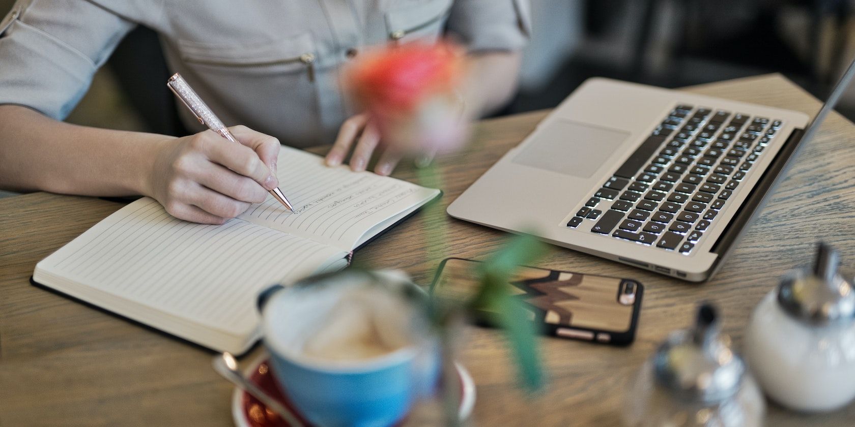 Une personne écrivant sur un carnet à côté d'un MacBook.