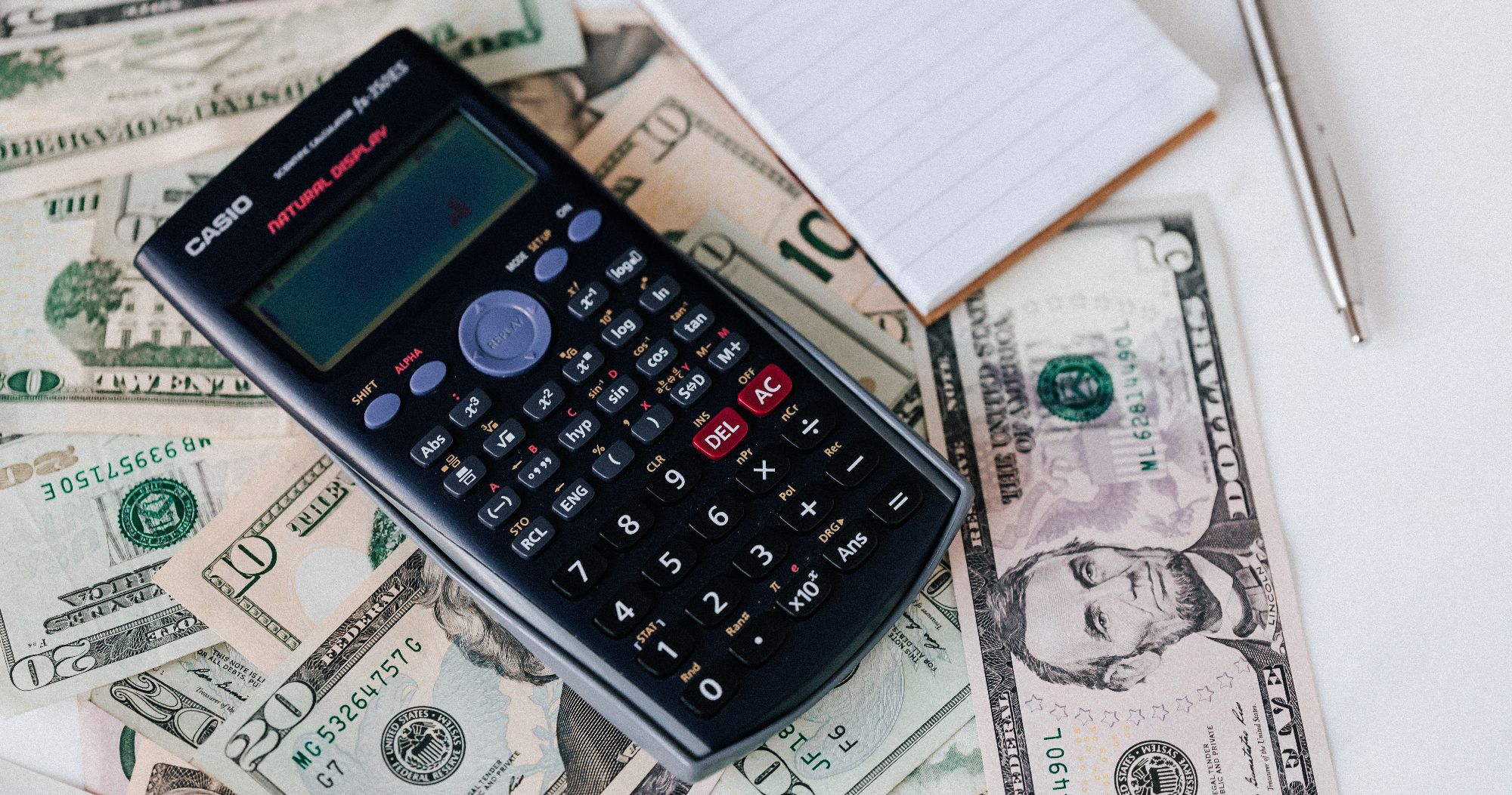 kalkulator dan notepad di atas uang
