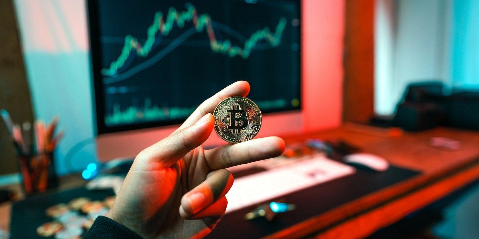 A hand holding a digital coin beside a trading chart