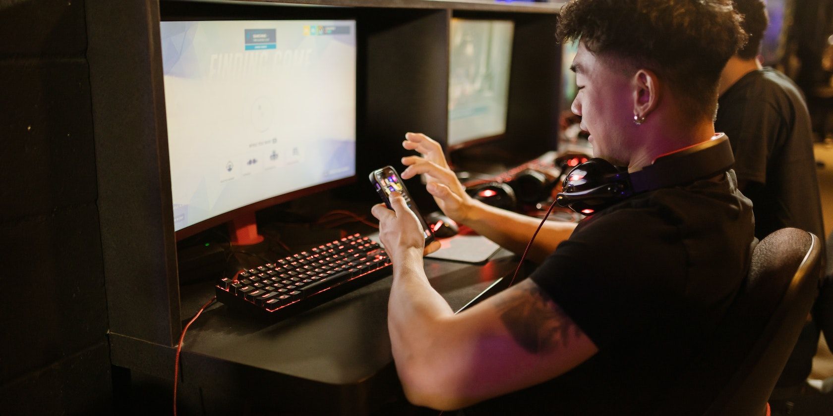 Man in Black Shirt Using a Smartphone while Sitting by the Gaming Computer