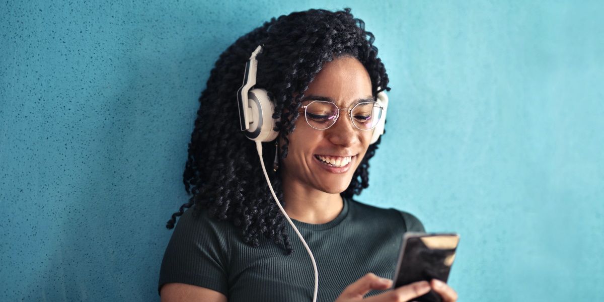 wanita tersenyum dengan kacamata mendengarkan audio di ponselnya menggunakan headset putih