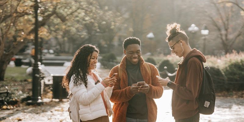 Three people holding their phones in a park and smiling 
