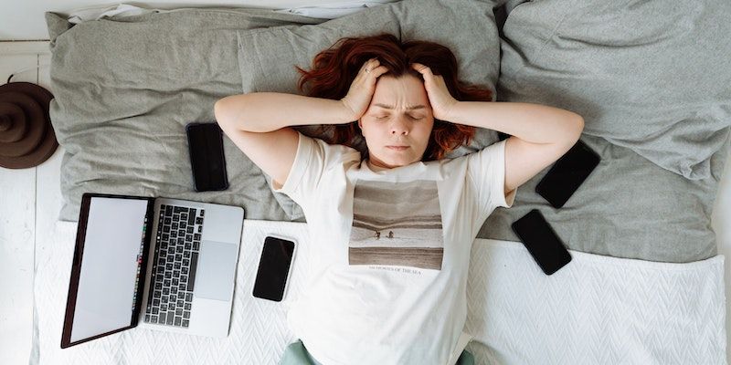 Một người phụ nữ kiệt sức nằm trên giường với máy tính xách tay và điện thoại bên cạnh