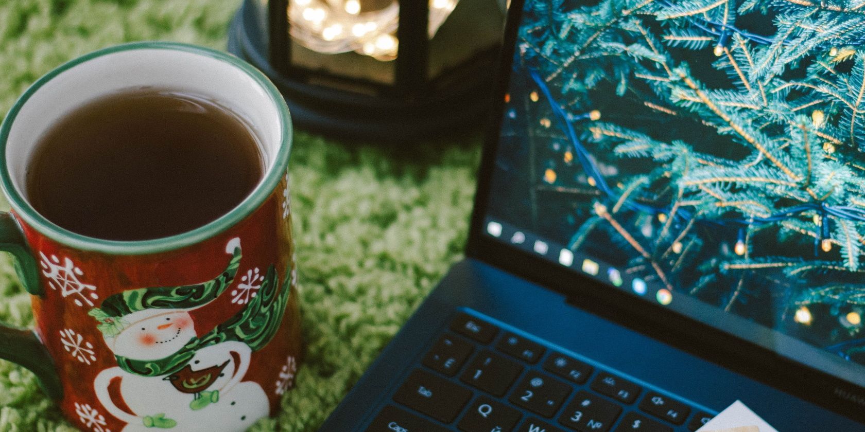a laptop sitting on grass with a christmas mug next to it