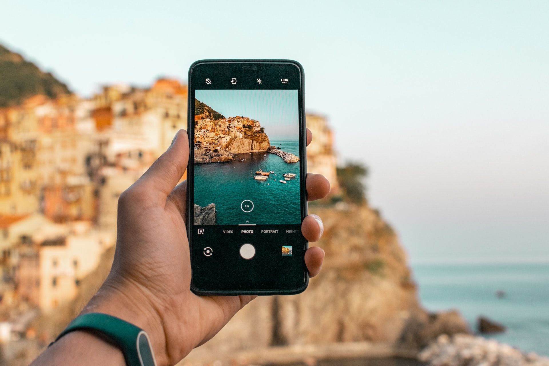 A hand holding an iPhone taking a portrait photo of a coastal village.