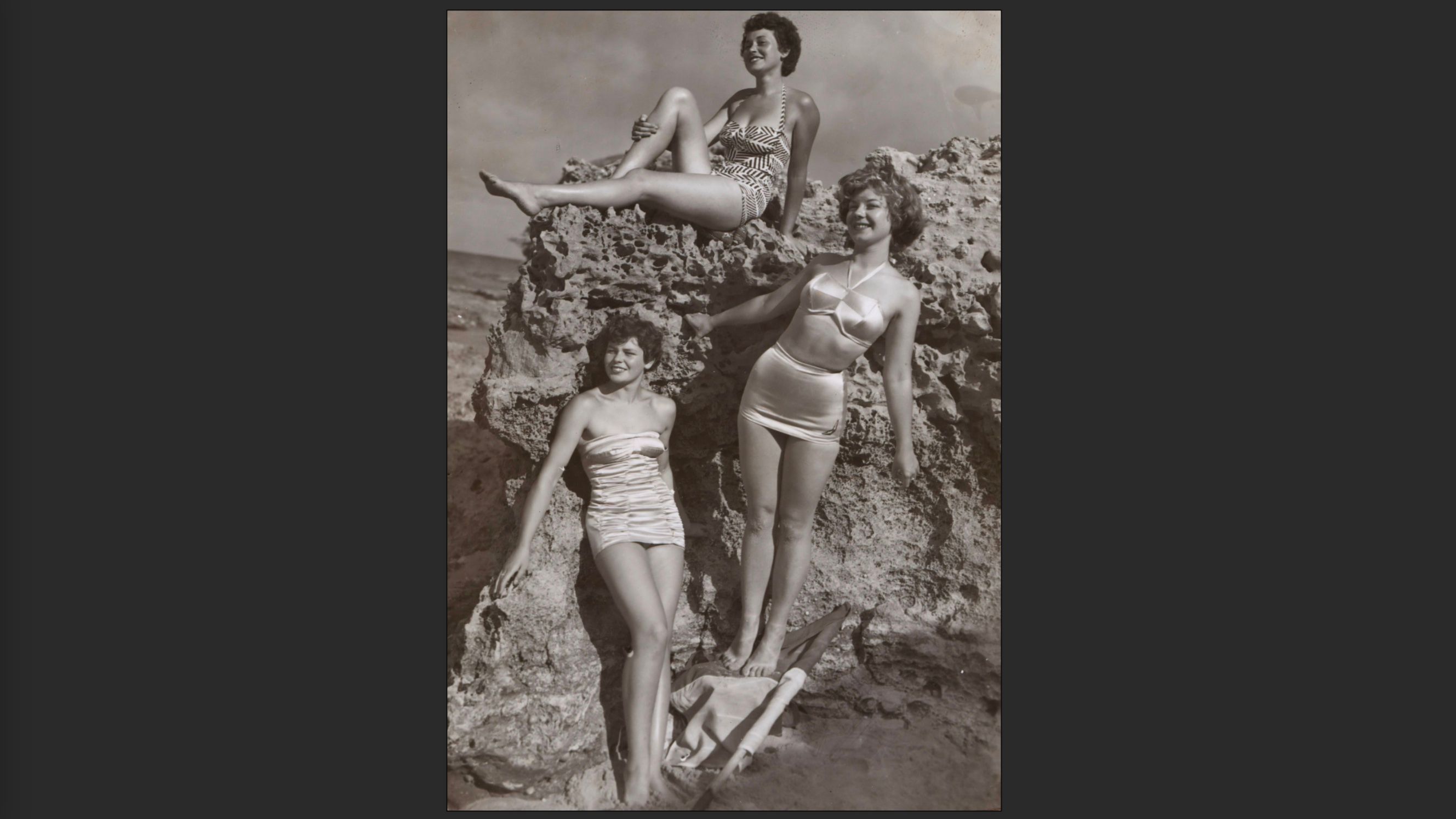 Three woman in bathing suits on a rock, black and white, portrait orientation