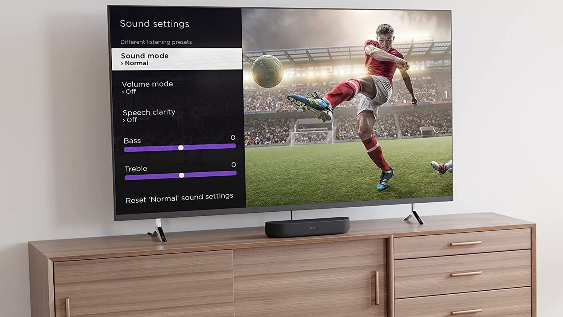 Roku Streambar روی پایه تلویزیون چوبی زیر تلویزیون نصب شده نشسته است