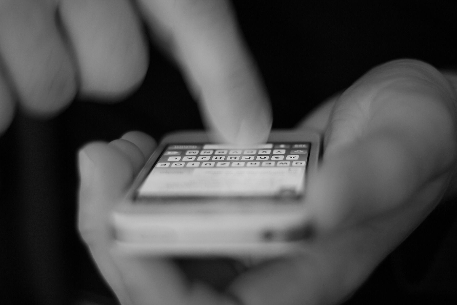 Foto hitam putih seorang pria mengetik di smartphone