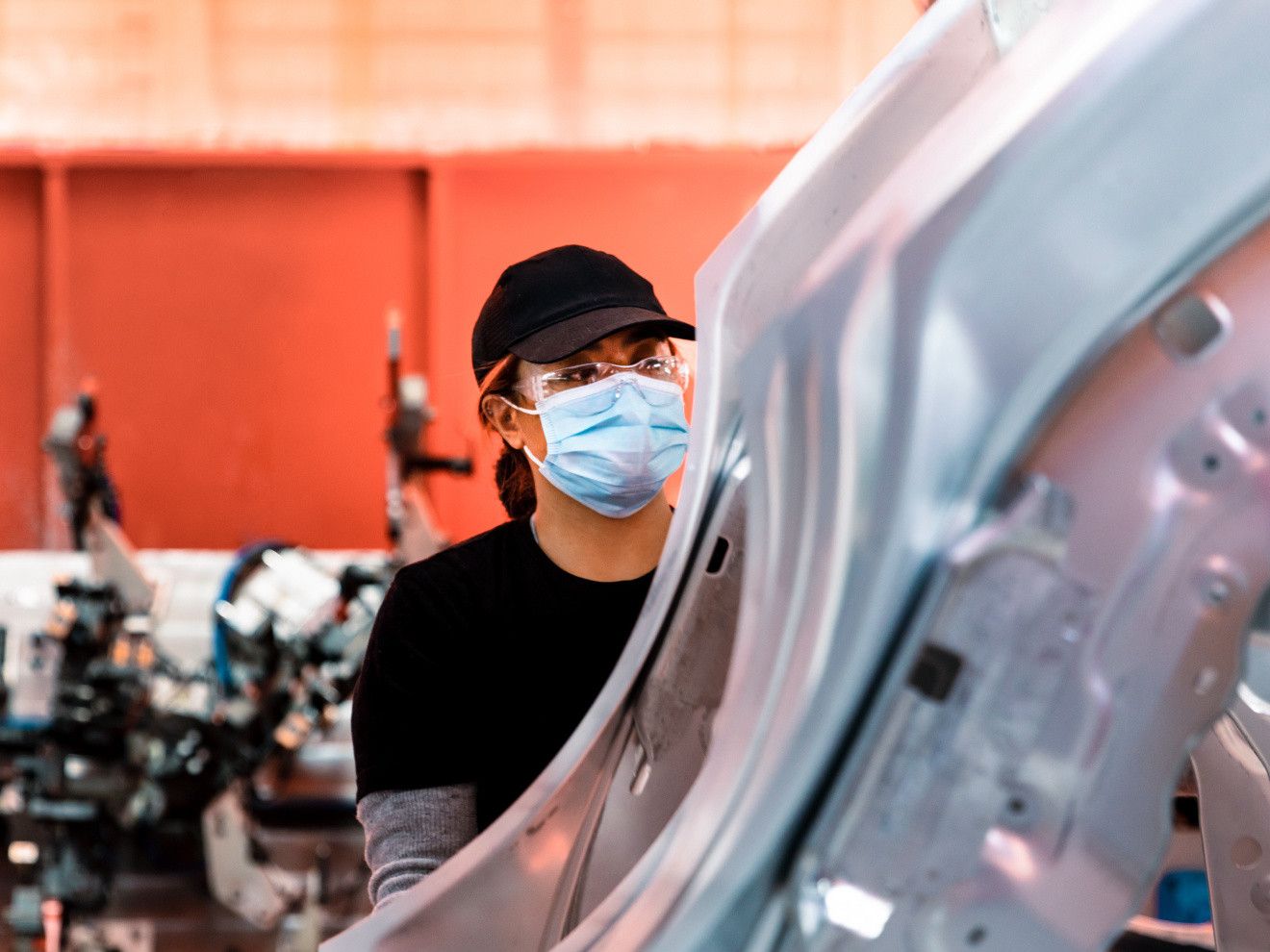 A masked technician examines a Tesla