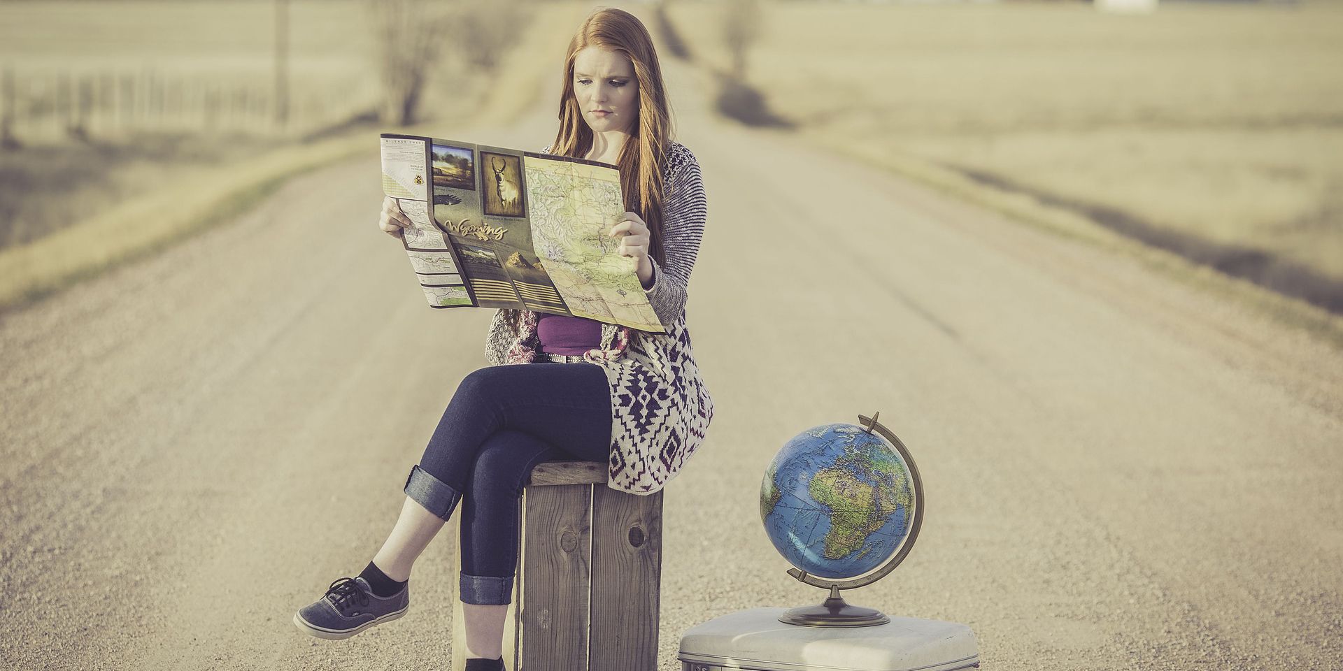 Bavulun üzerinde oturan ve yolun ortasında harita okuyan bir bayan