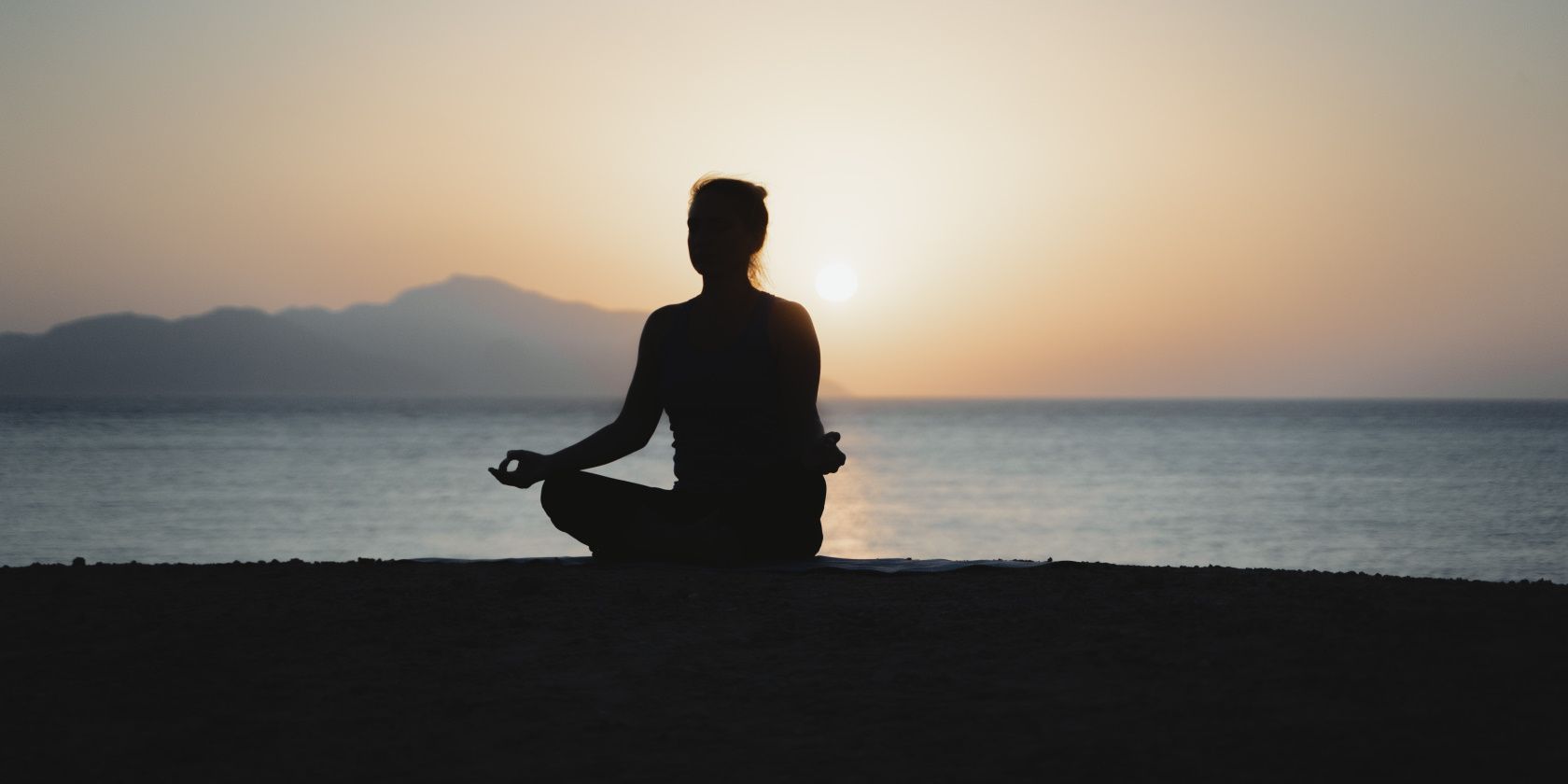 woman meditating on a beach at sunset