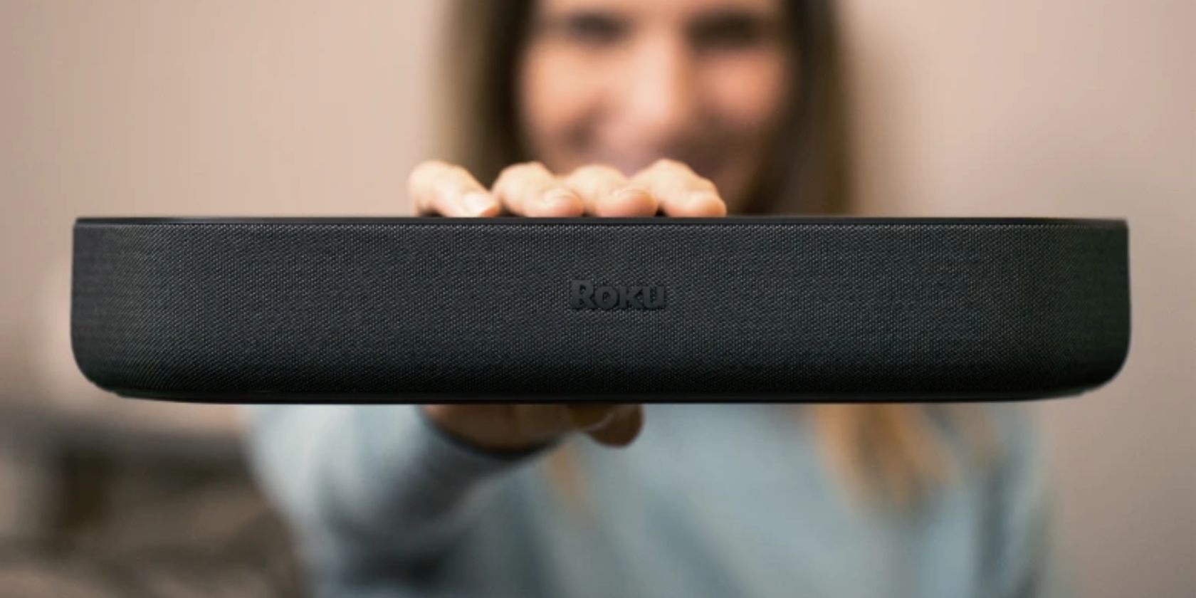 Woman standing out of focus holding up Roku Streambar