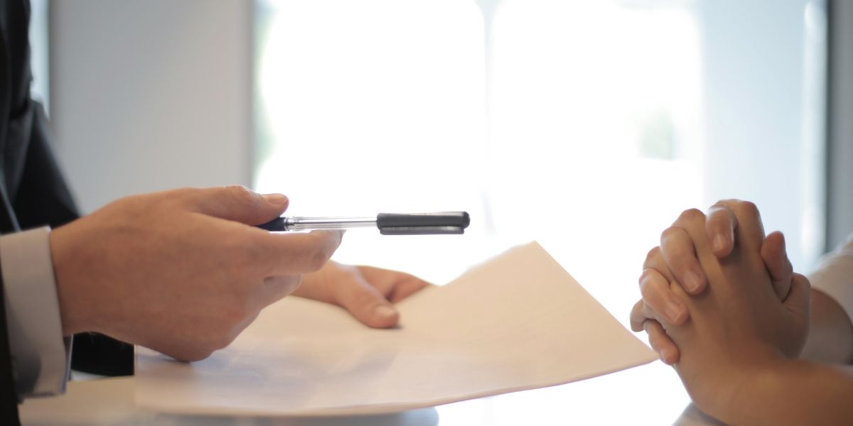 man holding out a pen and paper for signature