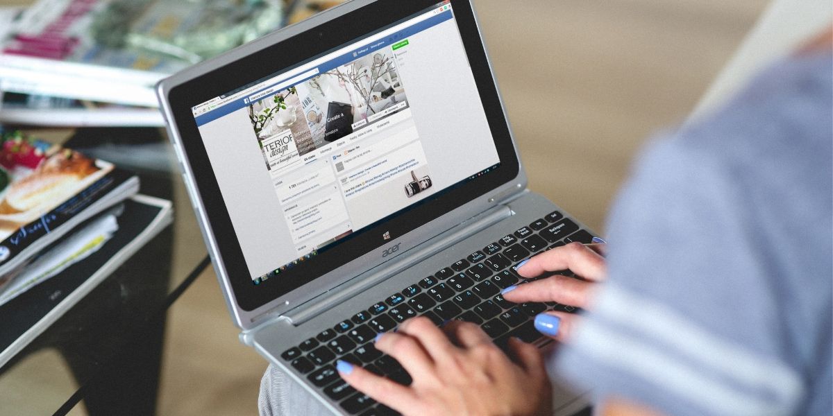 woman typing on a laptop showing a facebook profile