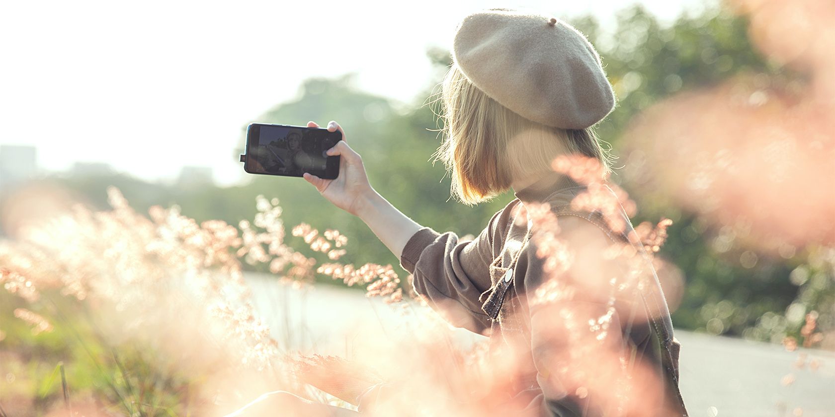 Woman in field taking selfie on phone.