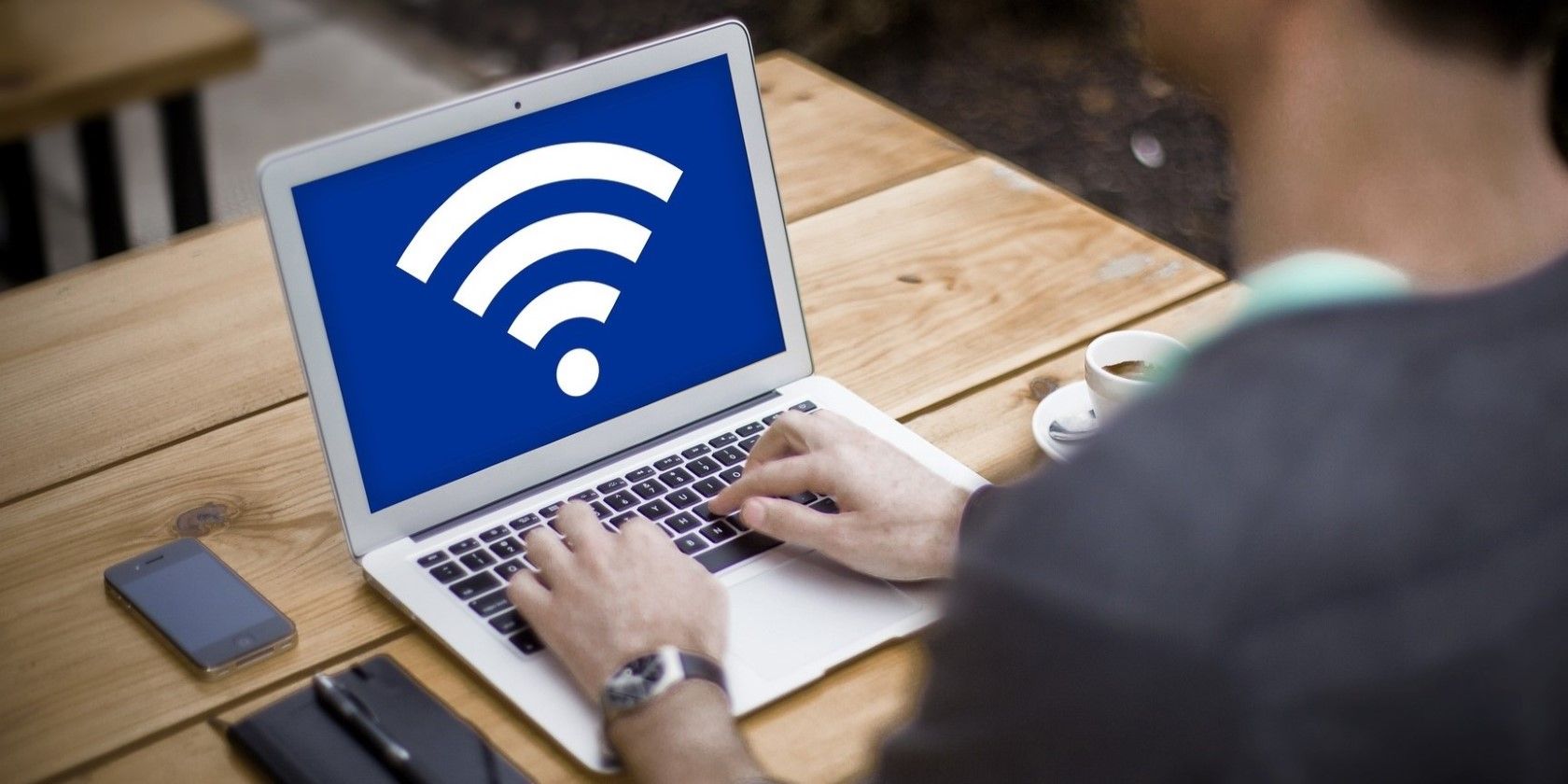 A man using a silver laptop with a Wi-Fi symbol on it