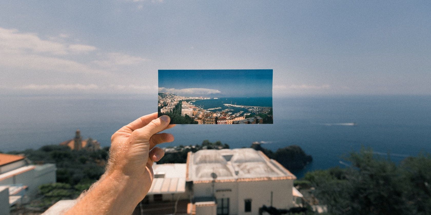 A hand holding a photograph infront of an ocean view
