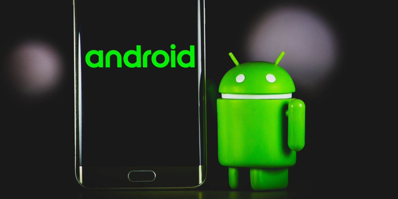 Android Berdiri di Samping Layar Smartphone Menampilkan teks android