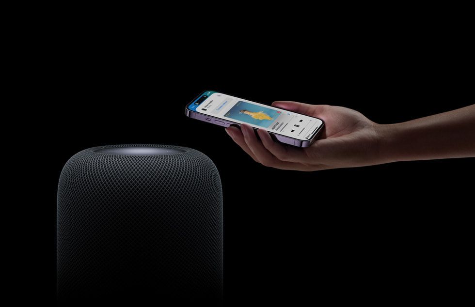 Hand holding an iPhone next to Apple HomePod