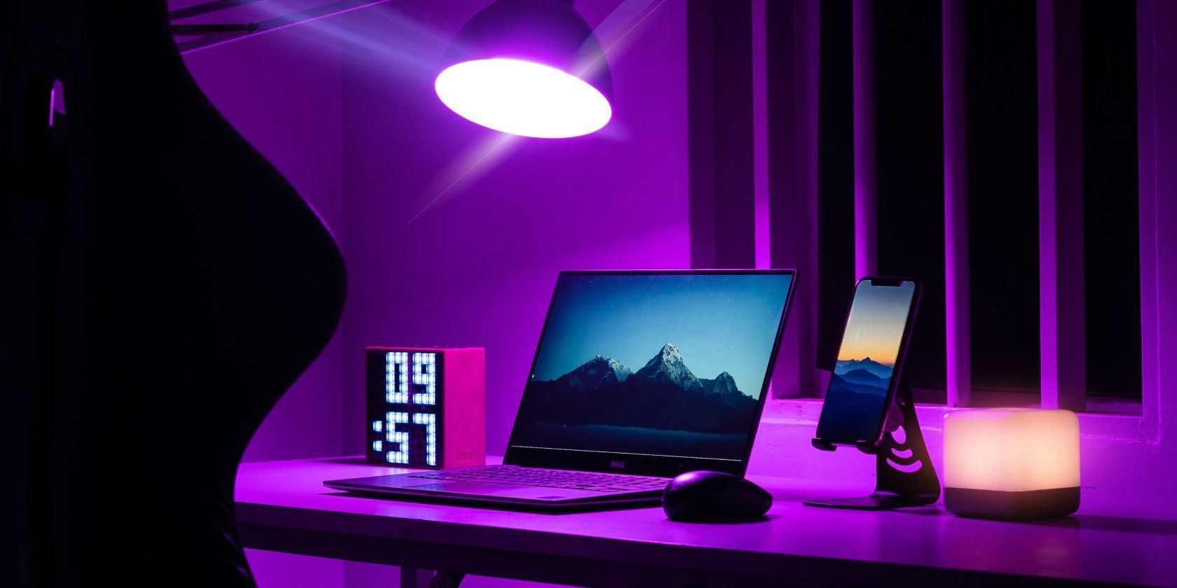 un ordinateur portable à côté d'une souris, d'un téléphone, d'une horloge et d'une souris, éclairé par un éclairage violet
