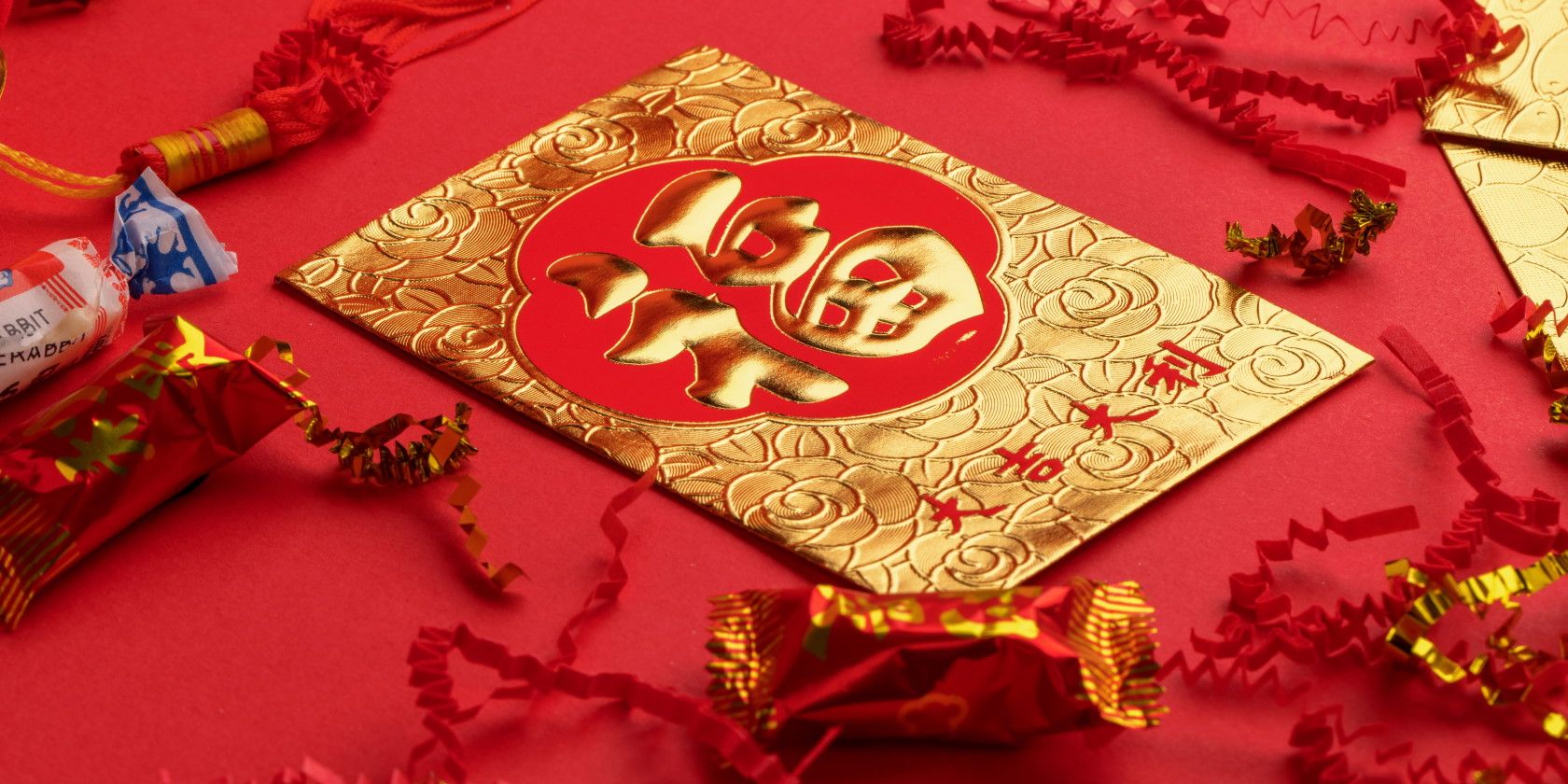 Gold and red Chinese New year letter on red tablecloth surrounded by chinese candy