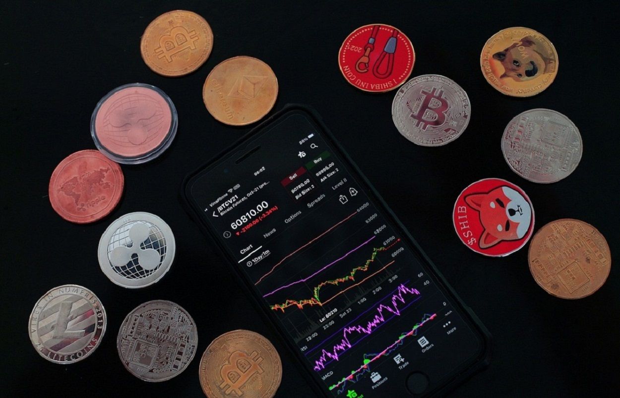 A smartphone showing a BTC chart with several cryptocurrencies around it.