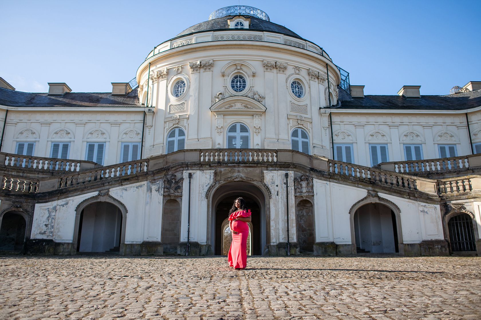 Pregnant woman standing in front of grand building.