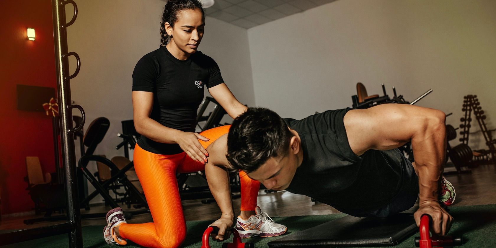 fitness coach assisting person doing push ups in a gym