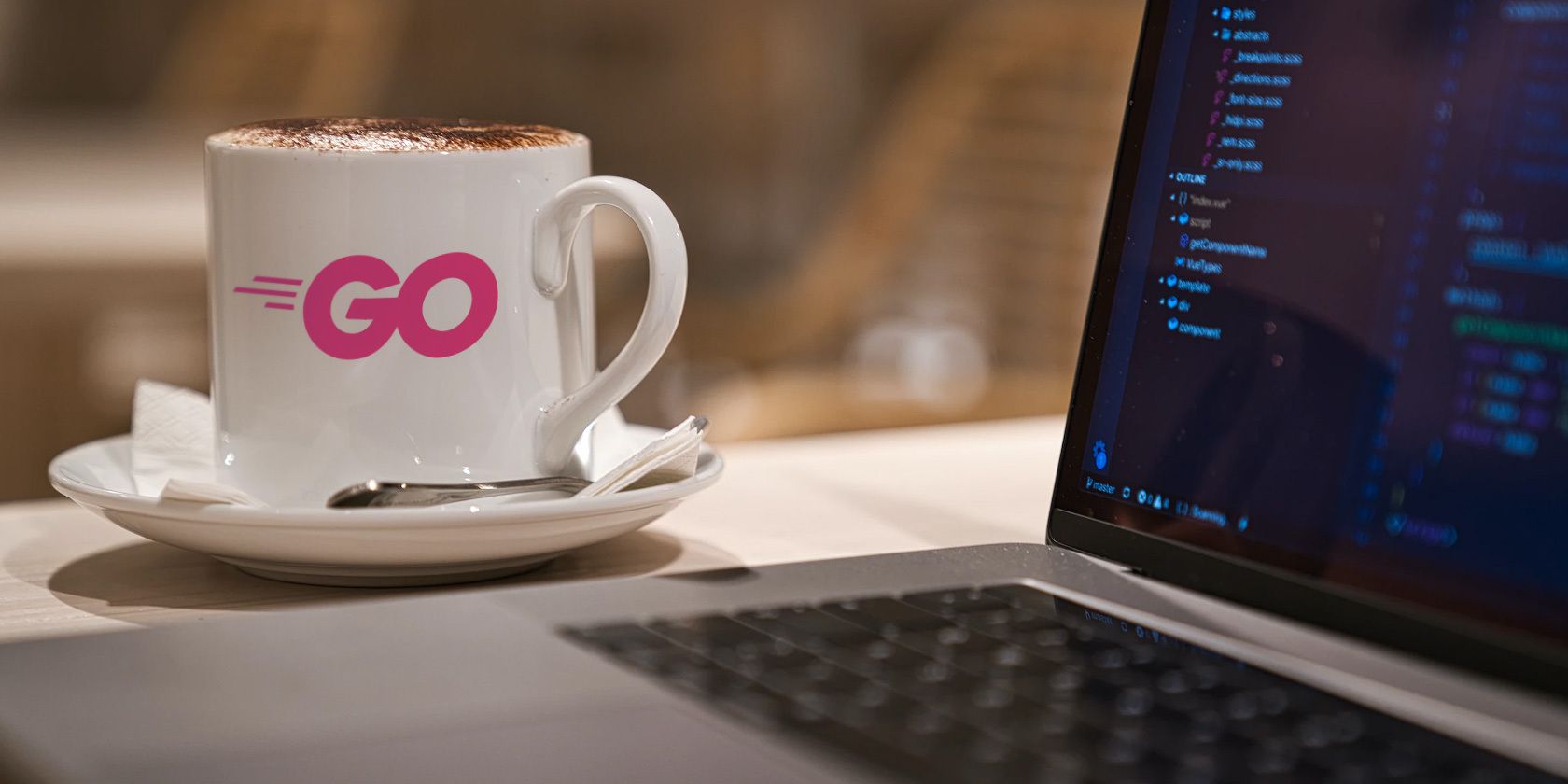 A partial view of a laptop in the foreground in front of a coffee cup with the Go logo on it.