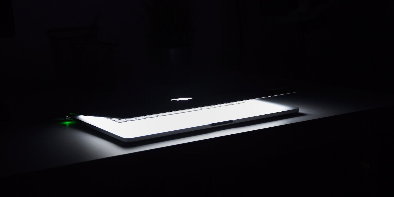 Half-closed MacBook glowing in a dark room