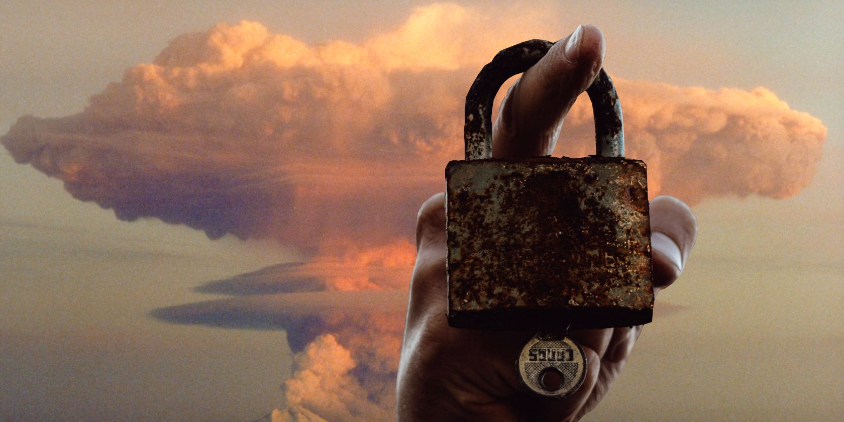 hand holding padlock on one finger in front of a mushroom cloud