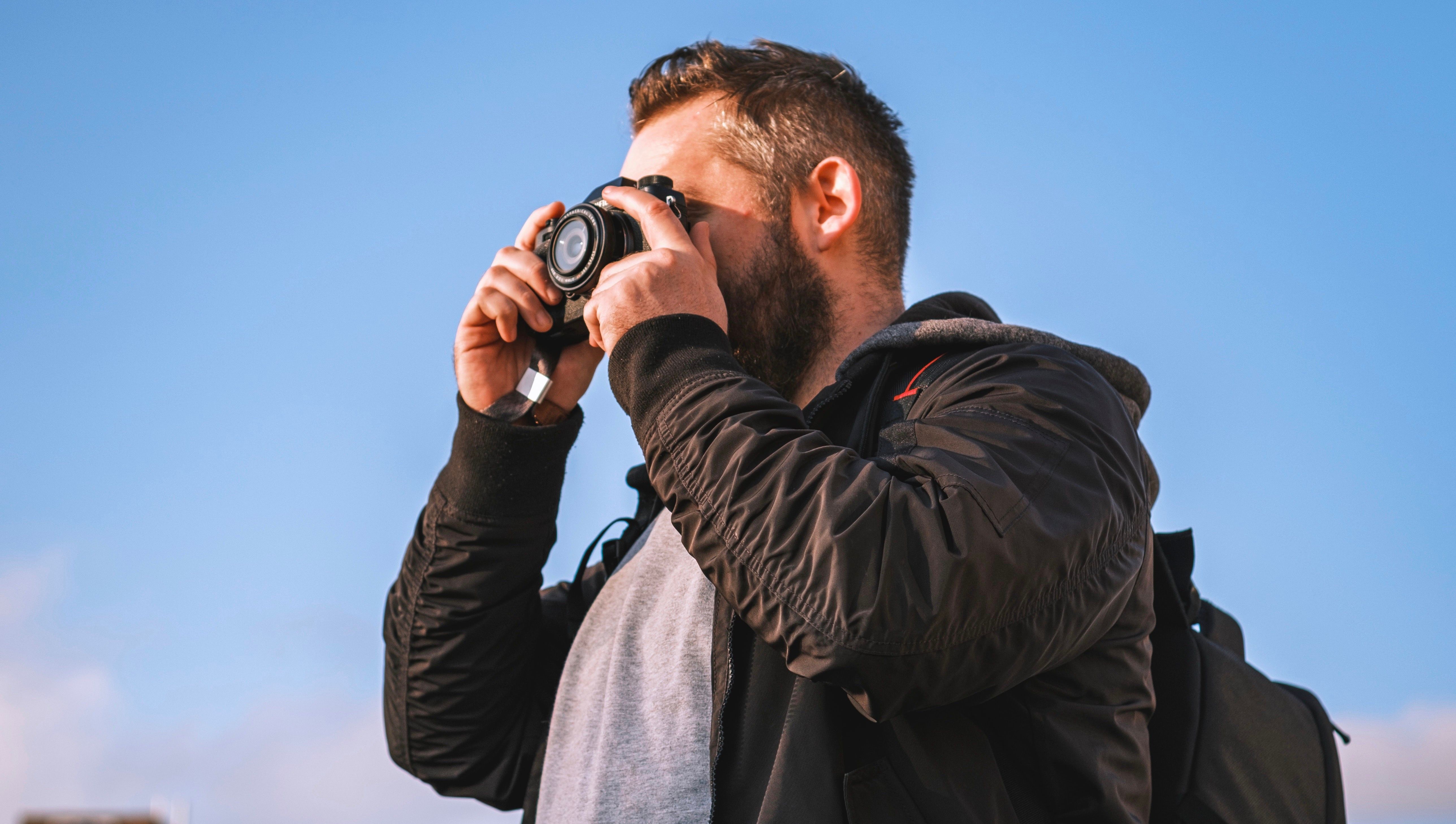 Man holding camera to face with blue sky behind him