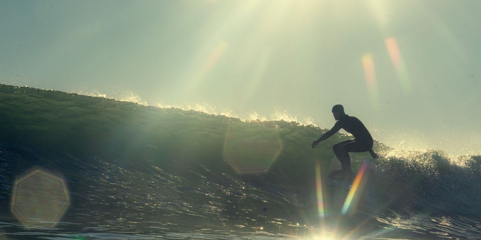 Photo of a person surfing with lens flare in the image