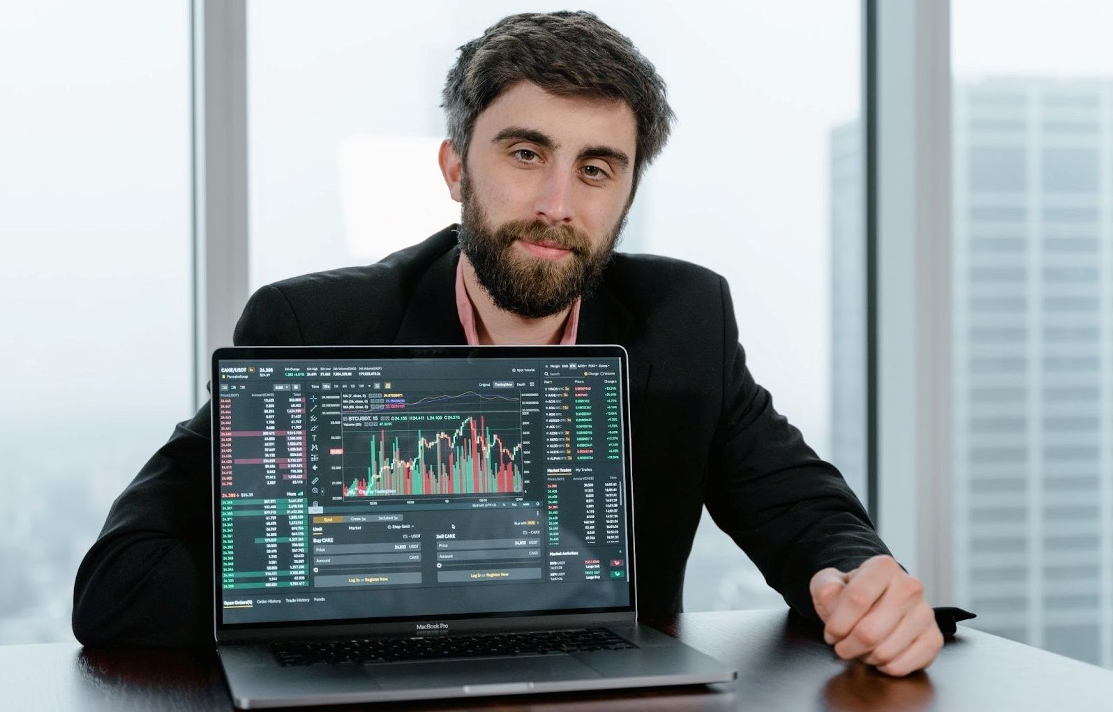 A man sits behind a laptop screen showing a crypto price chart