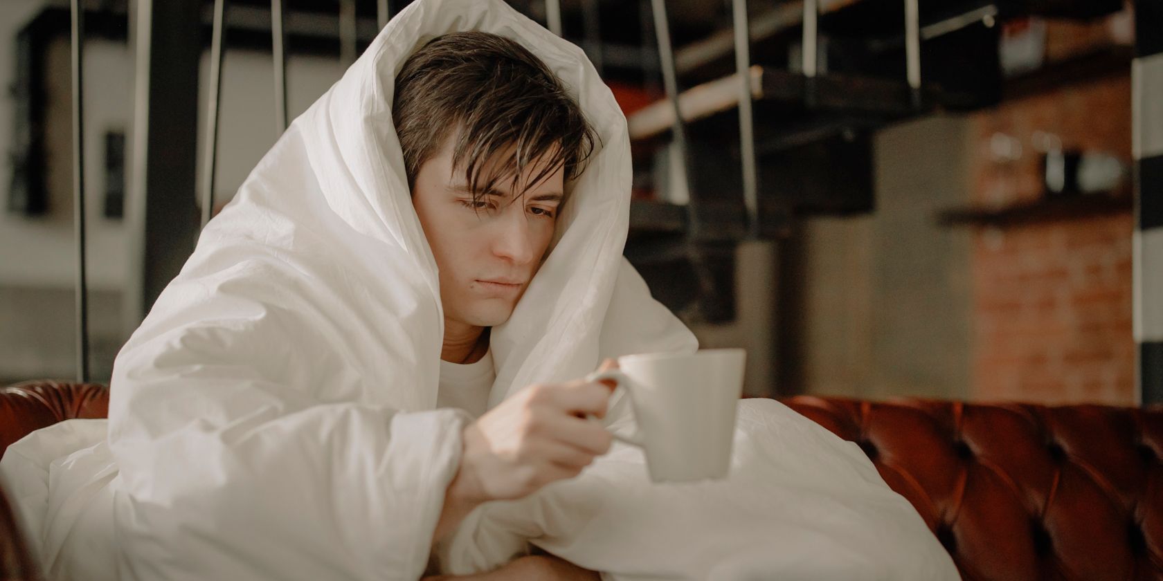 Man with flu wrapped in a quilt holding a hot drink