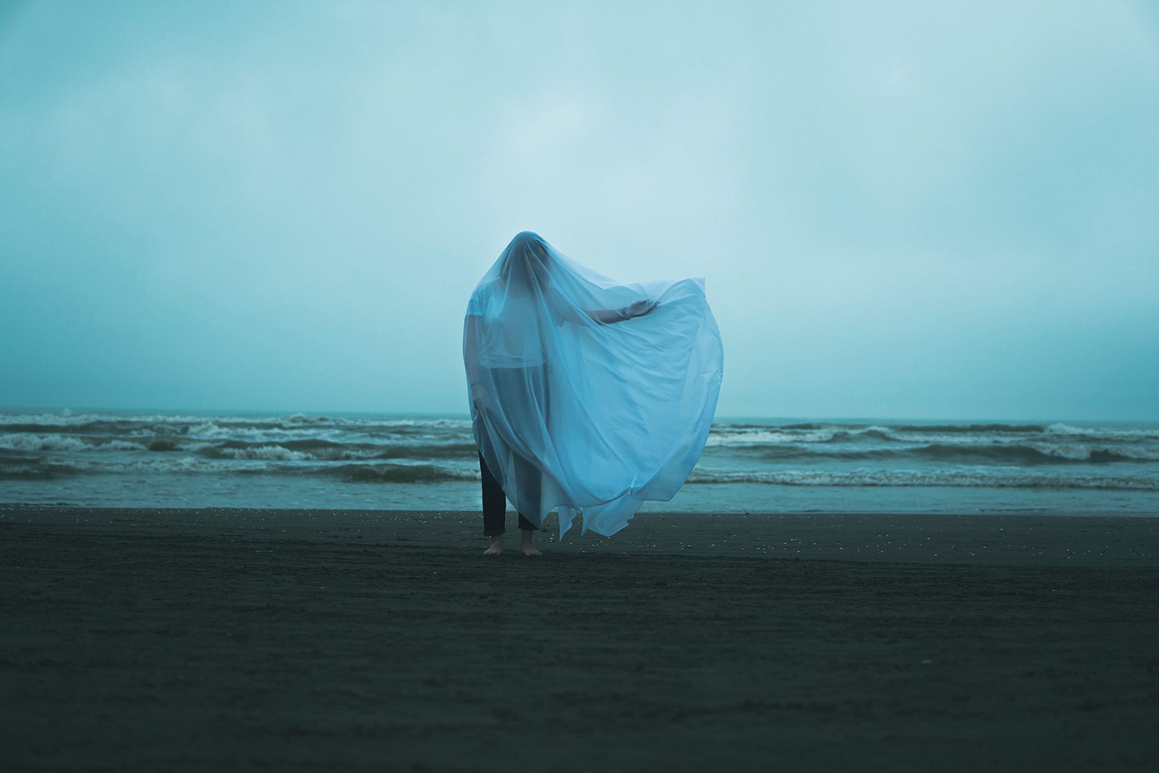 Man on beach covered in sheet.
