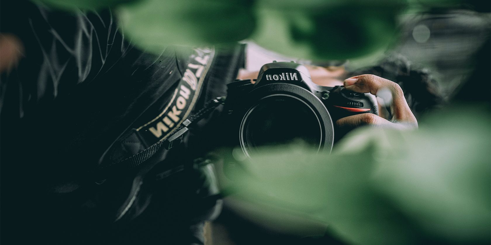 Photographer holding Nikon camera in greenery.