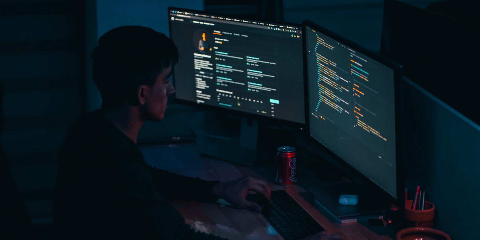 Person coding in a dark room in front of three monitor screens