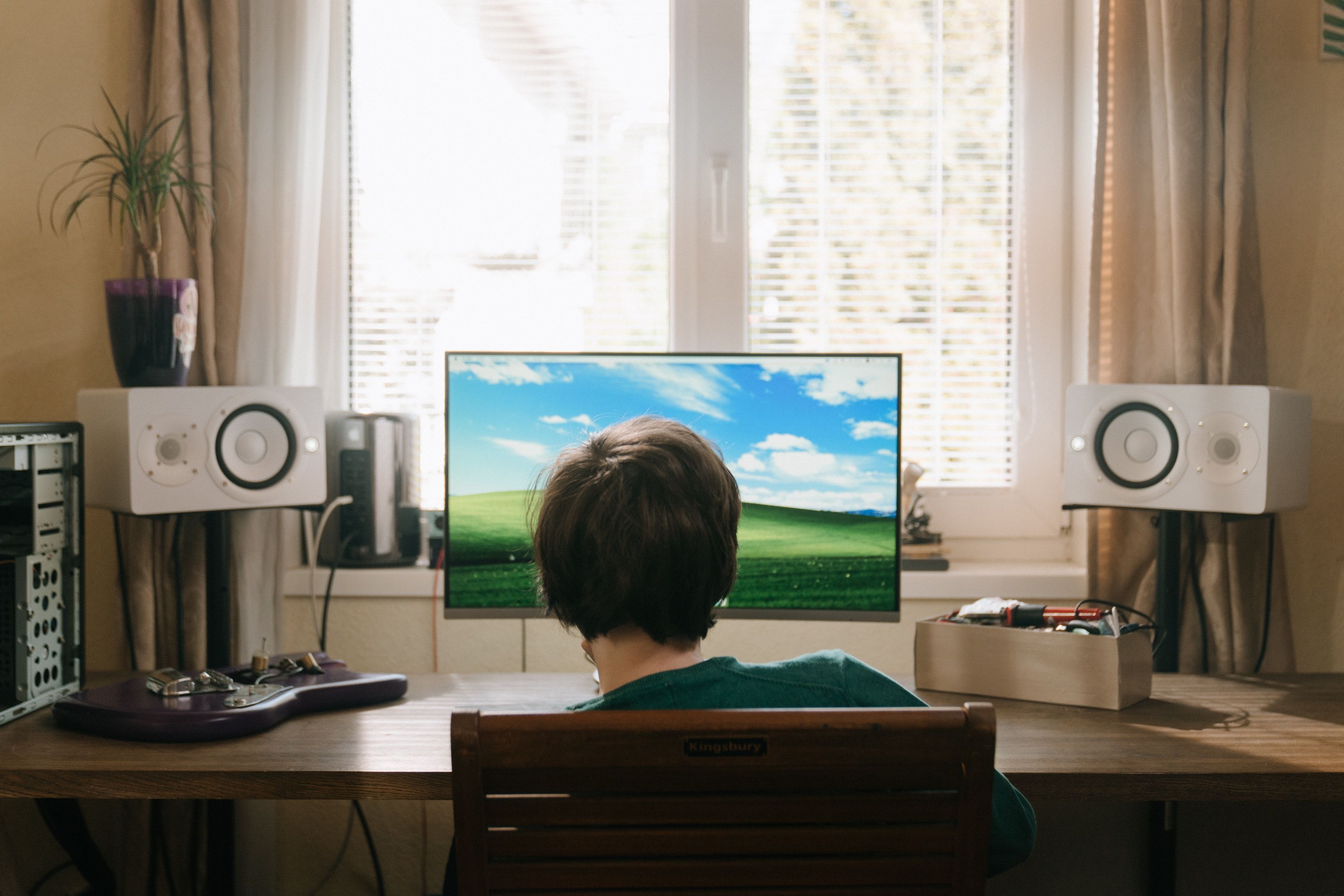 A boy in a red shirt sitting on a chair in front of a black flat screen television