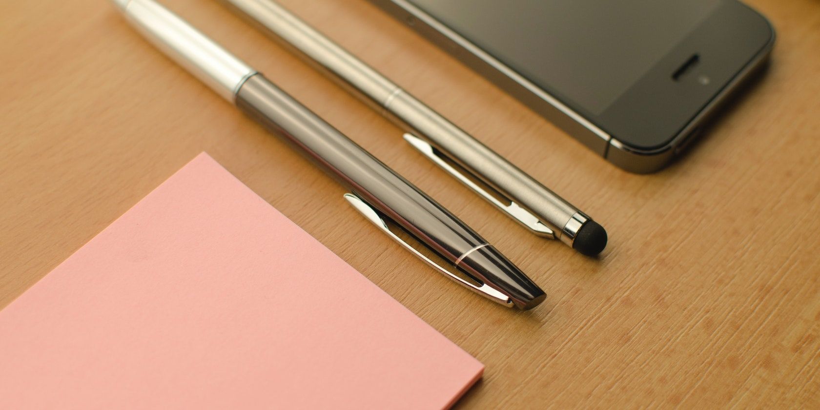 pens and notepad beside iPhone on wooden table