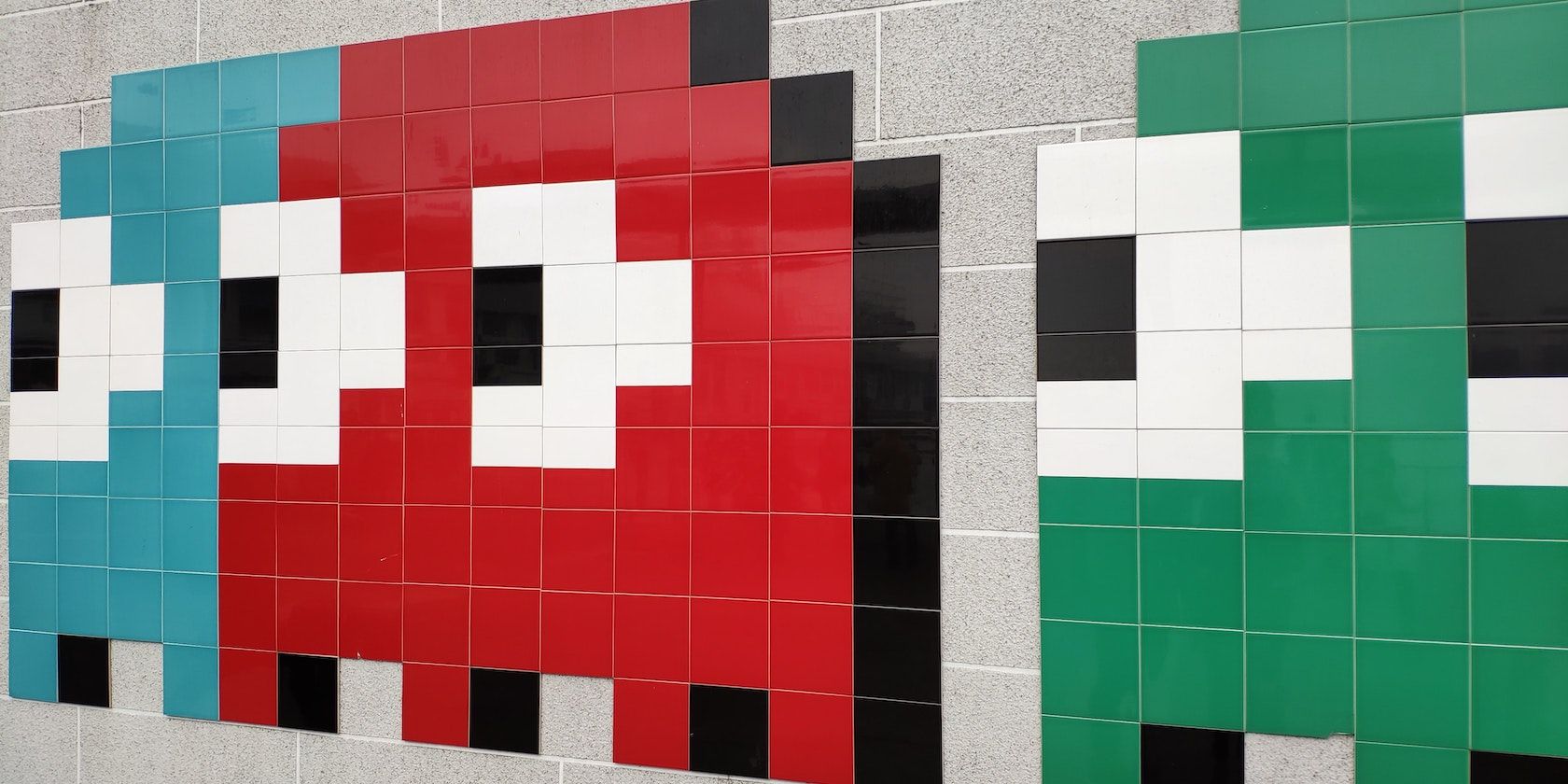 Large ghost characters from the game Pacman made from colored tiles on a wall.