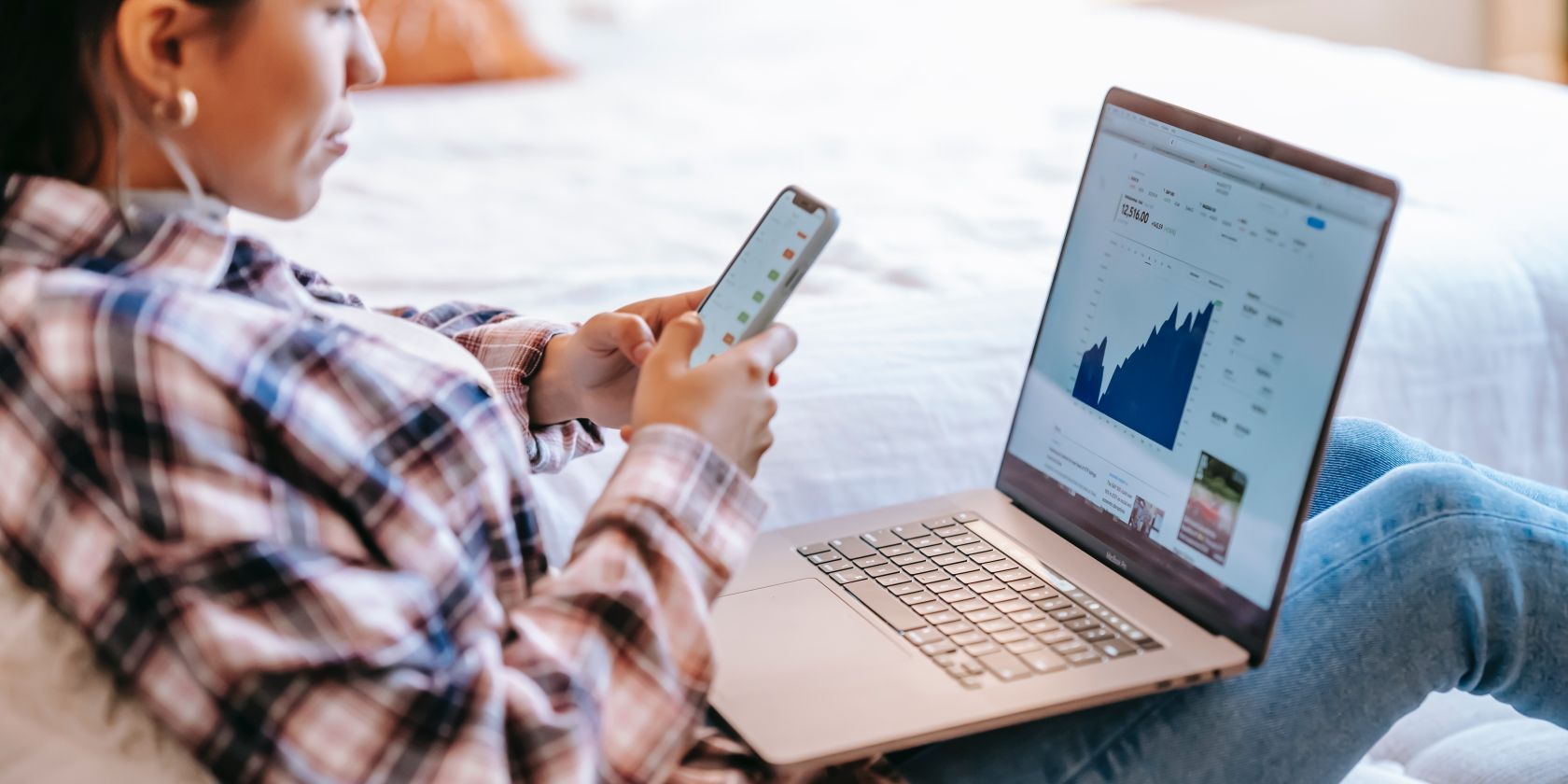 Woman Scrolling on iPhone with Laptop Resting on Lap