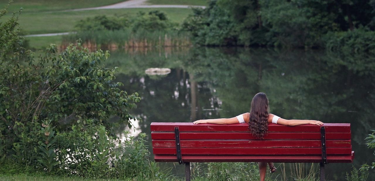 woman sitting on a bench next to a pond