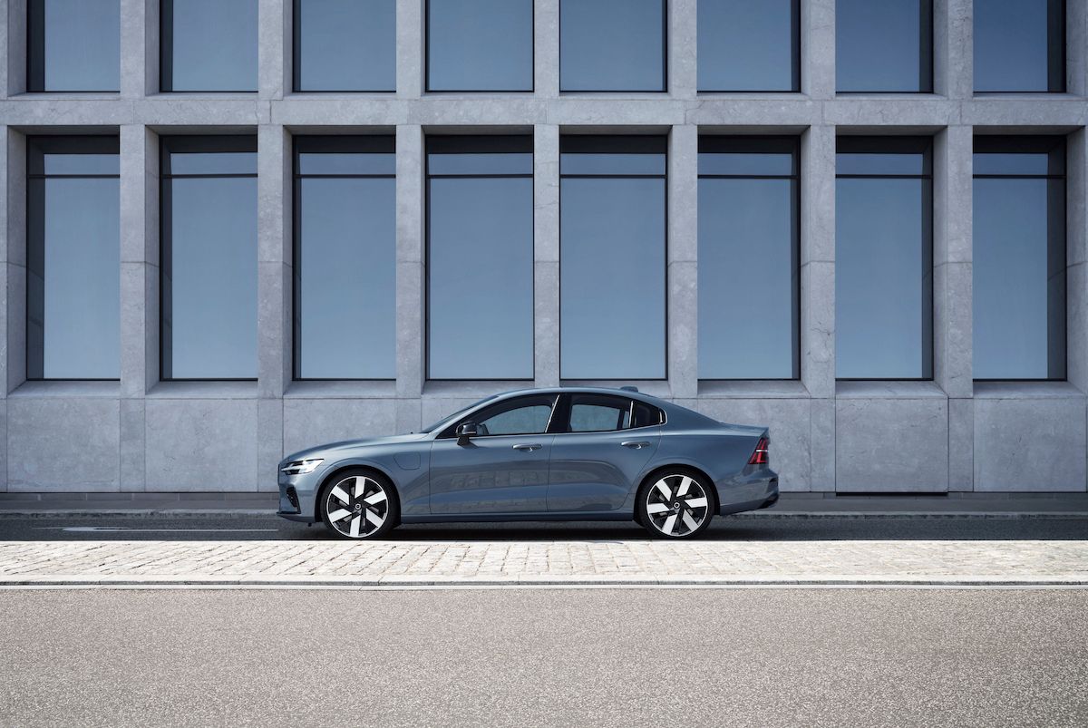 Mặt bên của chiếc Volvo S60 Recharge 2023 đậu bên ngoài một tòa nhà bằng kính