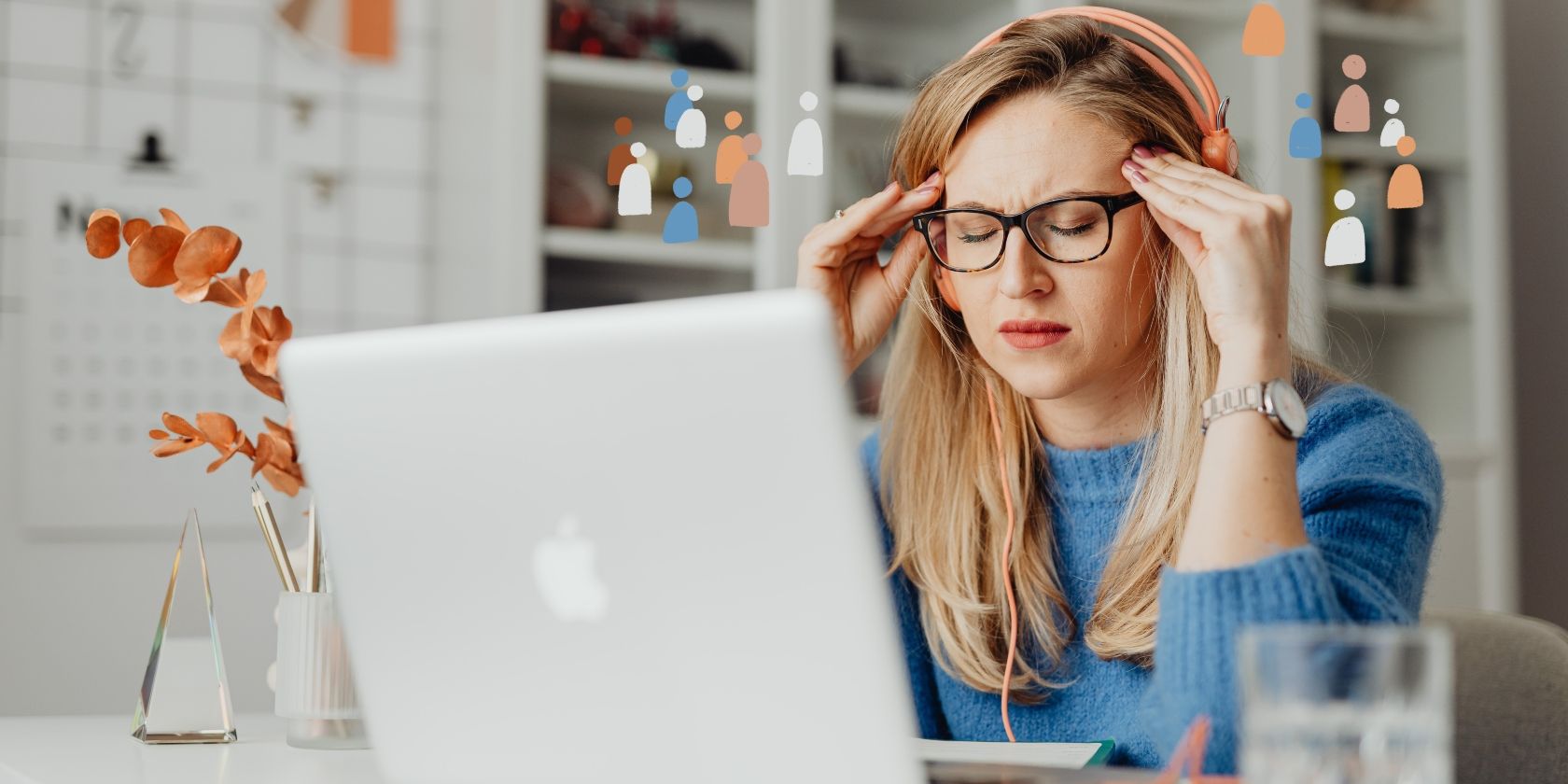 A frustrated woman in glasses and a blue sweater sitting in front of a MacBook
