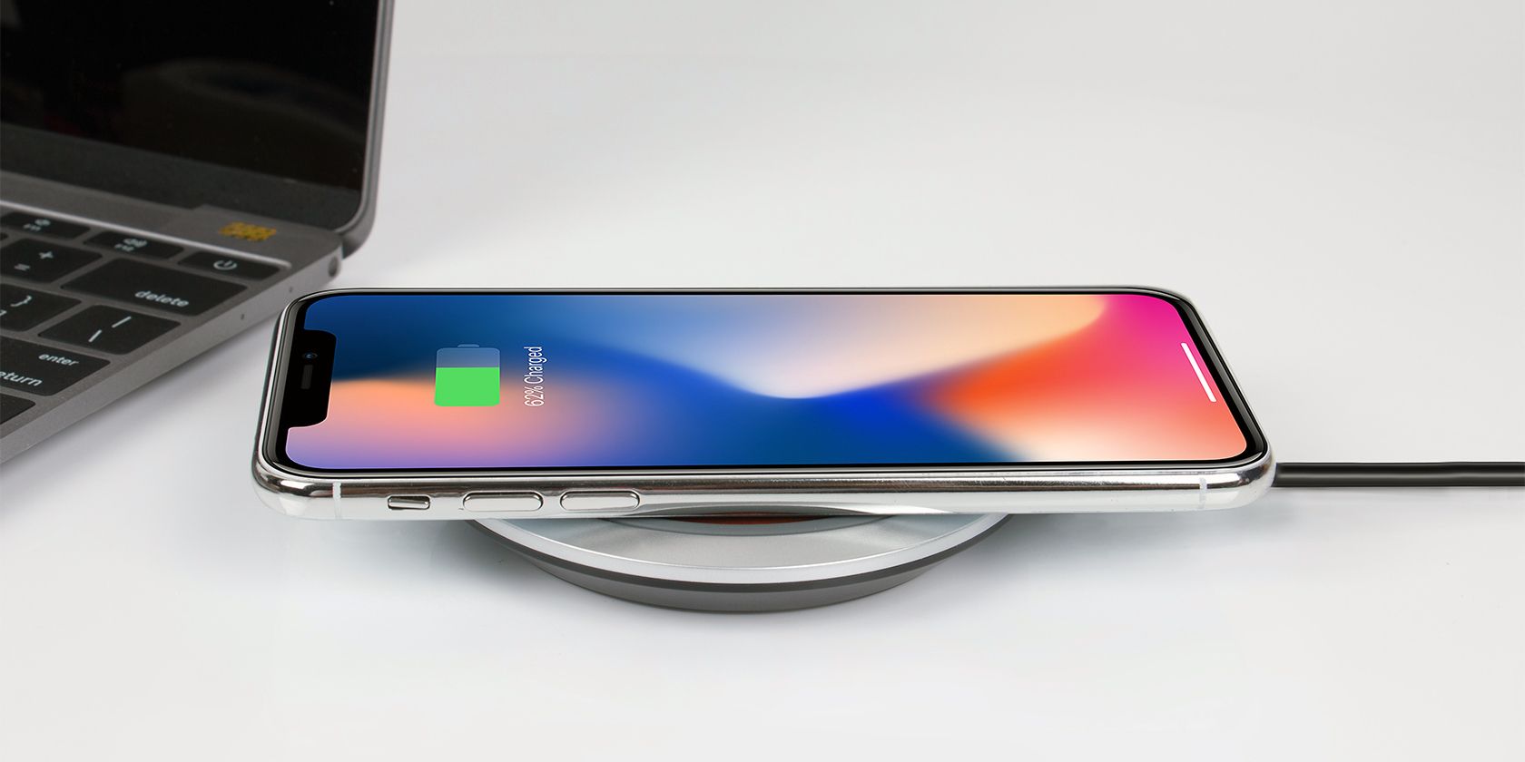 an iPhone wirelessly charging on a desk beside a laptop
