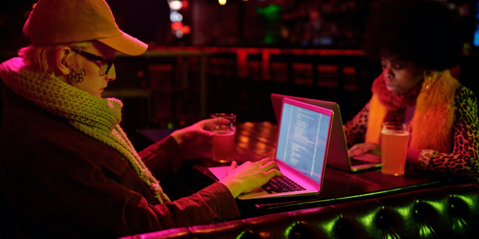 A man and a woman, facing each other, using their laptops in a bar