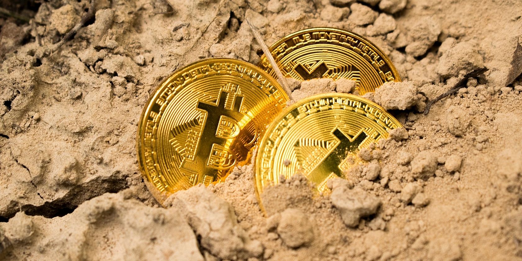 a picture of three bitcoin tokens in sand