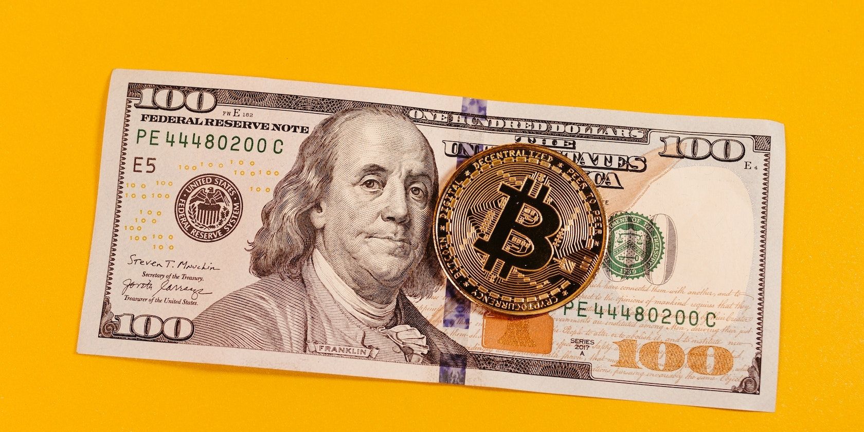a picture of bitcoin token and a hundred dollar note