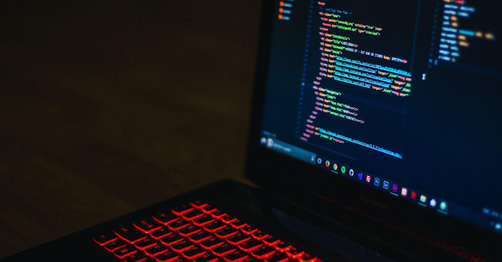 laptop di ruangan gelap dengan lampu latar keyboard merah dan kode di layar